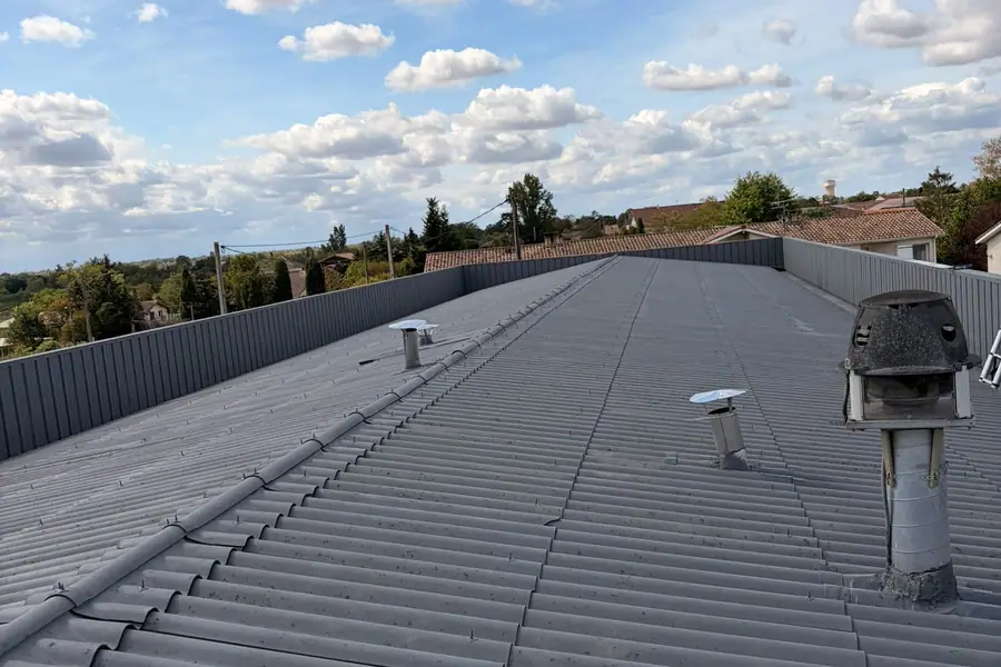 Grande couverture en bac acier gris ondulé avec sorties de ventilation en inox, sous un ciel de nuages