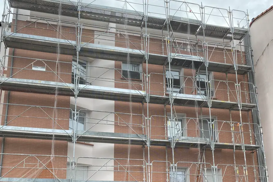 Immeuble en brique rose sous un échafaudage complet, avant ravalement de la façade