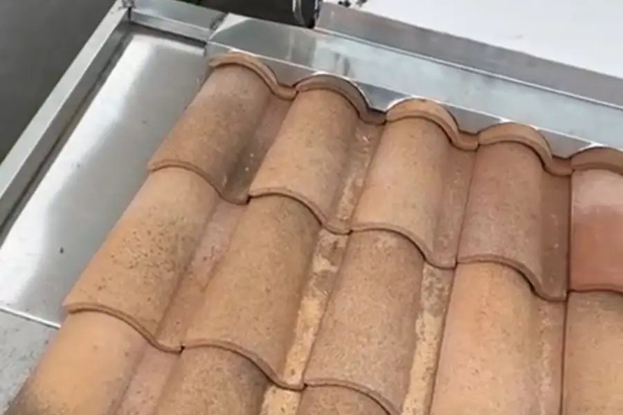Rive de tuiles romanes posée sur un chéneau en zinc neuf, garde-corps de balcon en arrière-plan